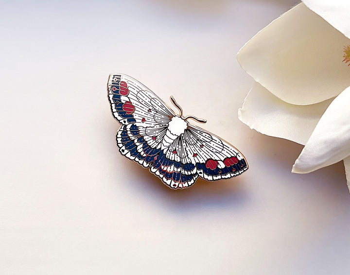Butterfly-shaped brooch with red and blue details on a white background